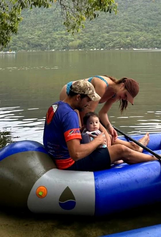 Leo Nardi Borba sentado no tubo de um raft azul na beira de uma lagoa, com a família